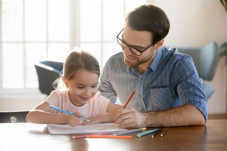 Young dad drawing pictures in paper album with small daughter.